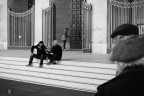 Ho scelto di includere le due figure a destra, nonostante l'ingombro, perch� fungono da quinta scenica. La loro presenza schiaccia la prospettiva e crea un effetto di 'spionaggio': non stiamo guardando una piazza aperta, ma stiamo sbirciando una conversazione privata da dietro le spalle di qualcuno.